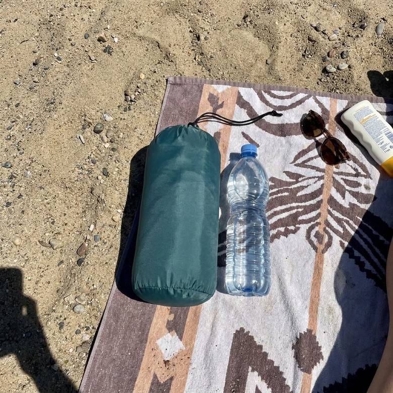 Gepackte Isomatte neben einer 1-Liter-Wasserflasche im Sand