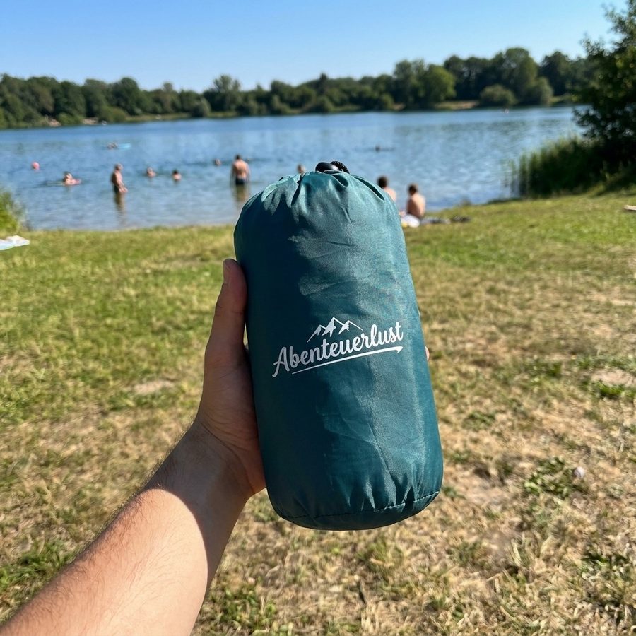 Packsack der Isomatte in einer Hand am Badesee
